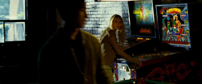 Abby playing pinball inside seedy pool hall.