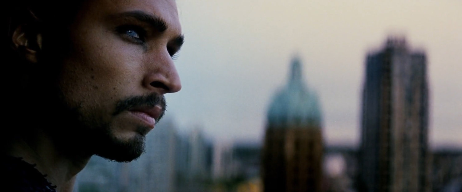 Tattoo on a high rise building, with other out of focus buildings behind him.