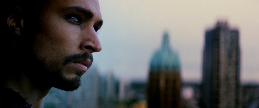 Tattoo on a high rise building, with other out of focus buildings behind him.