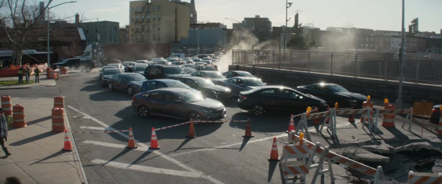 Cars stuck in a traffic jam by a large hole in the road.