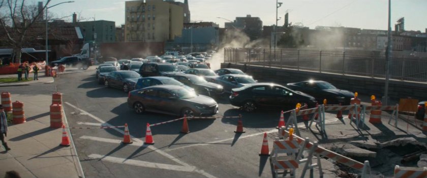 Cars stuck in a traffic jam by a large hole in the road.
