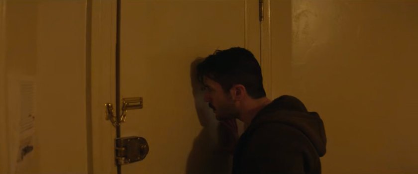 Nicky looking through the peephole of his apartment.