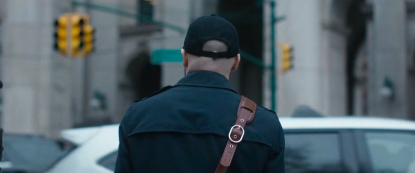 Interstitial: Man with hat and satchel standing by cars.