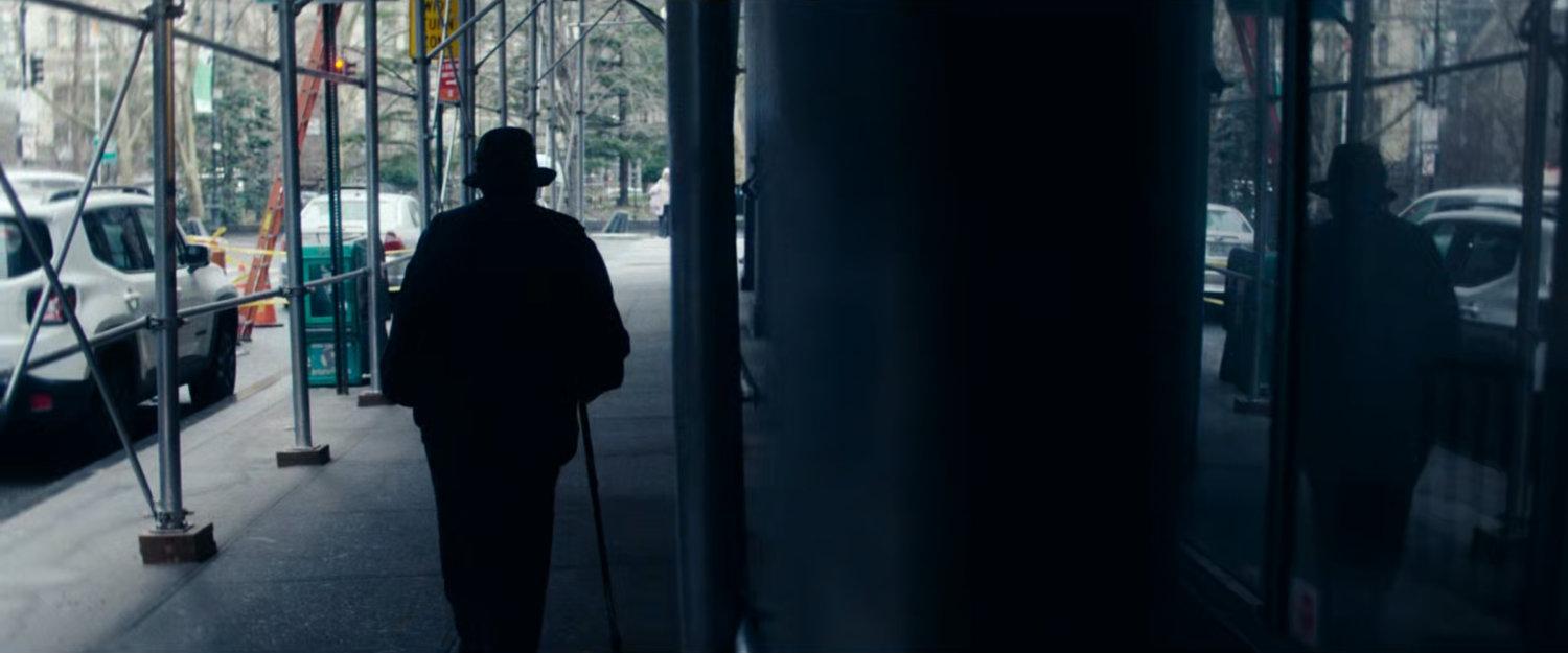 Interstitial: person walking on sidewalk under construction barrier, reflected in window.