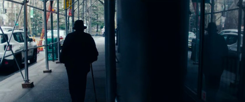 Interstitial: person walking on sidewalk under construction barrier, reflected in window.