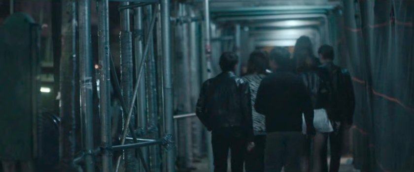 Interstitial: people walking on sidewalk at night under construction awning.