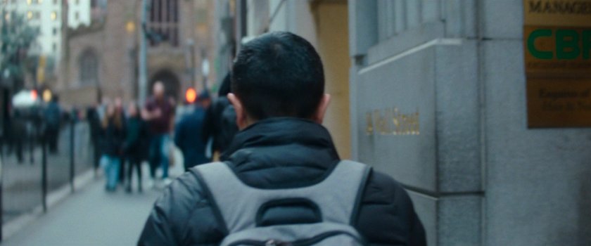 Interstitial: man with backpack on Wall Street sidewalk.