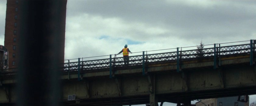 Interstitial: Worker in orange vest atop train bridge.