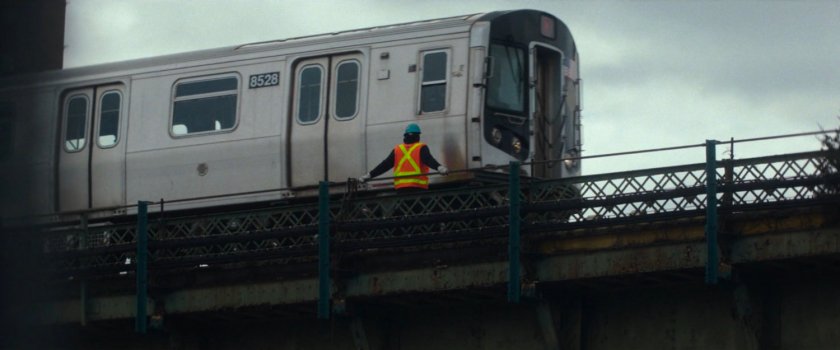 Interstitial: Worker in orange vest atop train bridge.