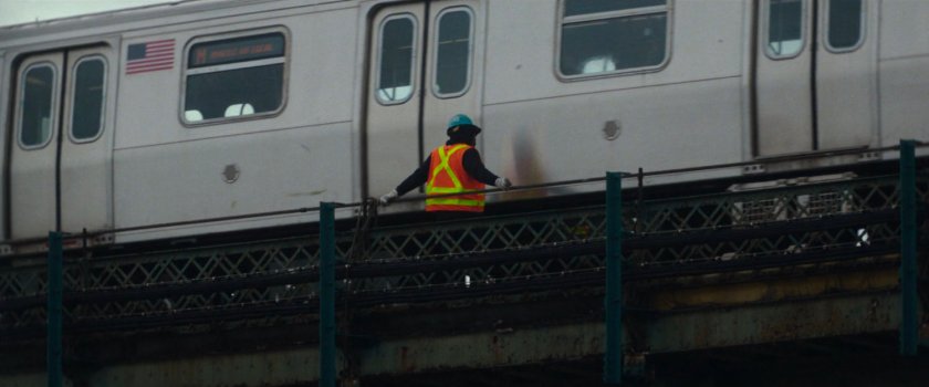 Interstitial: Worker in orange vest atop train bridge.