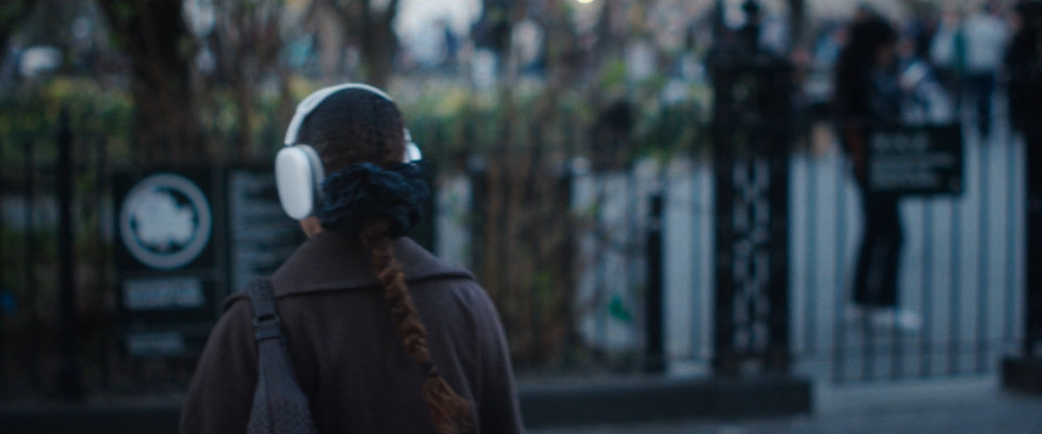 Interstitial: woman with white headphones near park.
