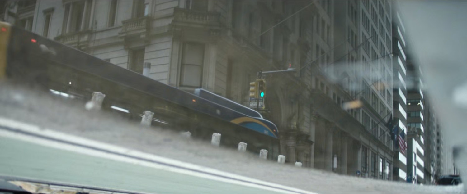 Interstitial: bus passing by building reflected in puddle.