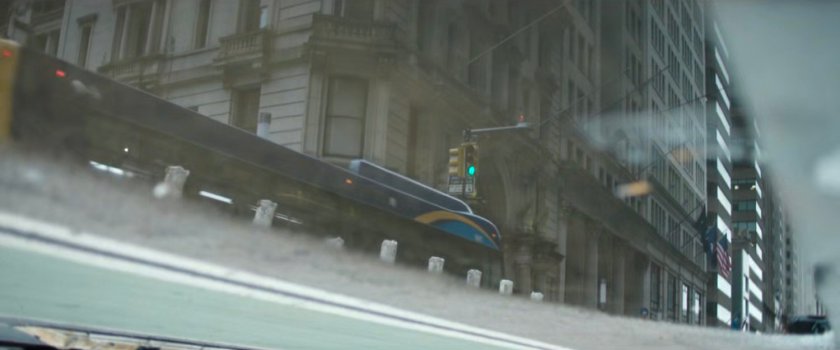 Interstitial: bus passing by building reflected in puddle.