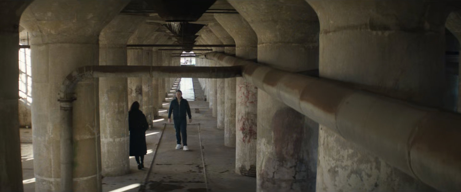 Luca walking towards Vanessa in abandoned grain terminal.