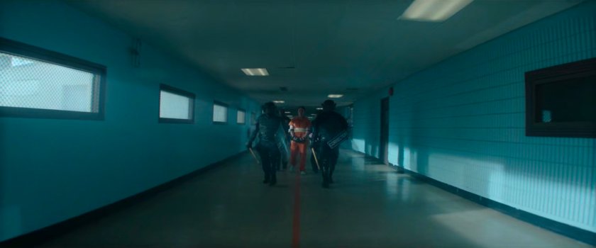 Guards walk Dex down hallway in Ryker's Island Penitentiary.