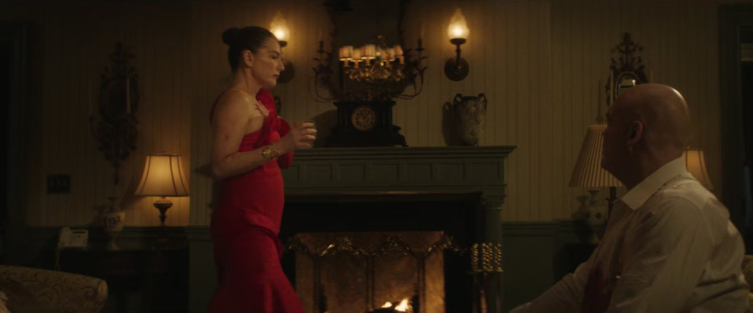 Vanessa standing next to the fireplace in their bedroom as Fisk watches her.