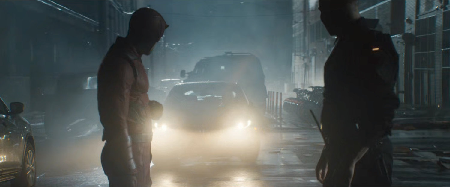Frank and Matt standing in front of car with headlights on outside Matt's apartment building.