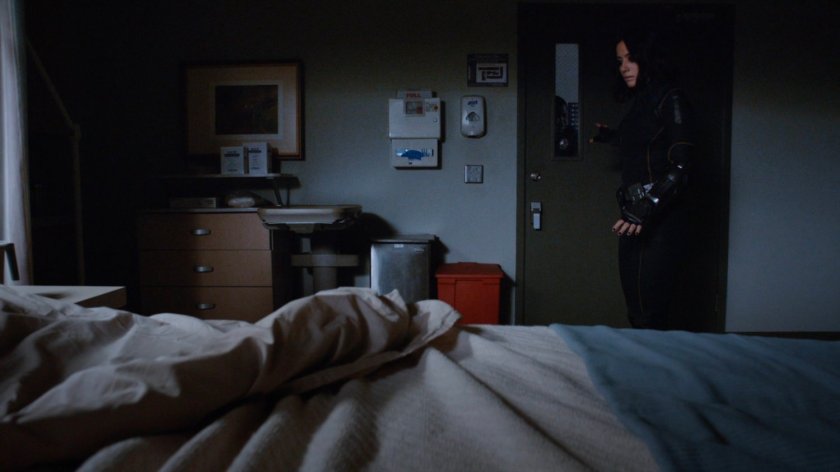 Daisy standing by Watchdog member laying in hospital bed.