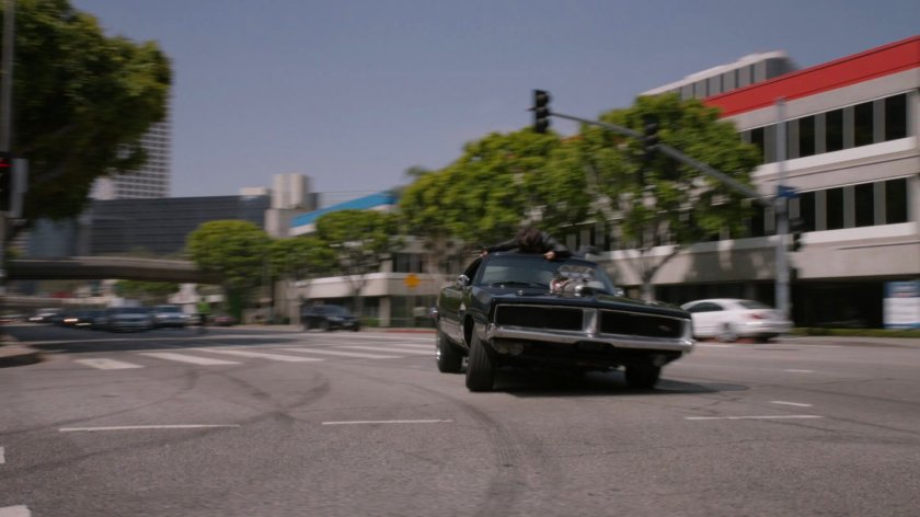 Daisy holding onto roof of Robbie's black Charger as it turns corner.