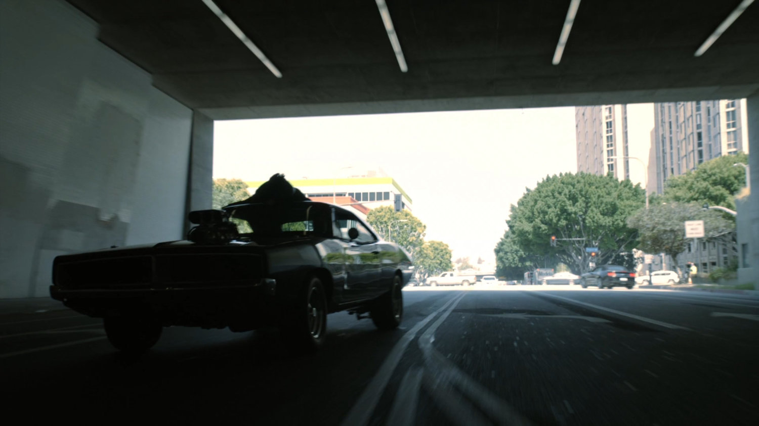 Daisy holding onto roof of Robbie's black Charger as it drives into tunnel.