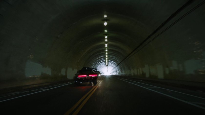 Daisy holding onto roof of Robbie's black Charger as it drives through tunnel.