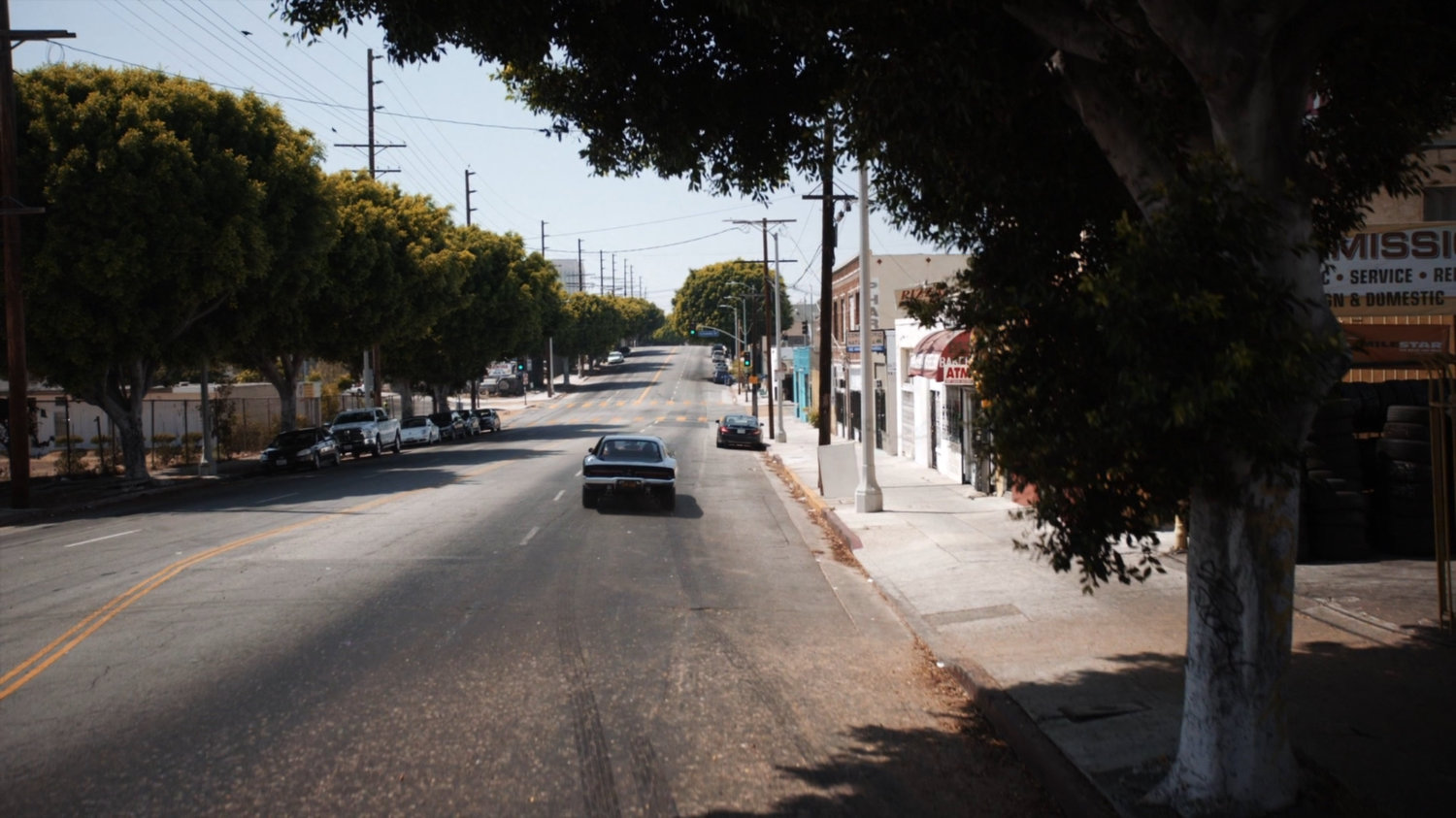 Robbie's black Charger driving away from Canelo's Auto & Body.