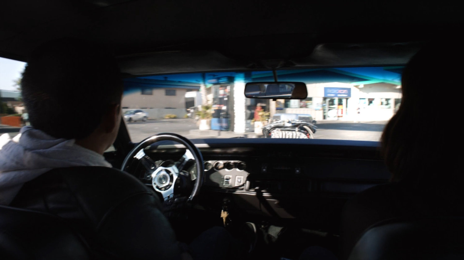 Interior of black Charger pulling into Roxxon station.