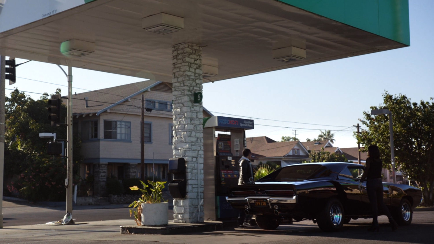 Daisy and Robbie outside black Charger at Roxxon gas station.