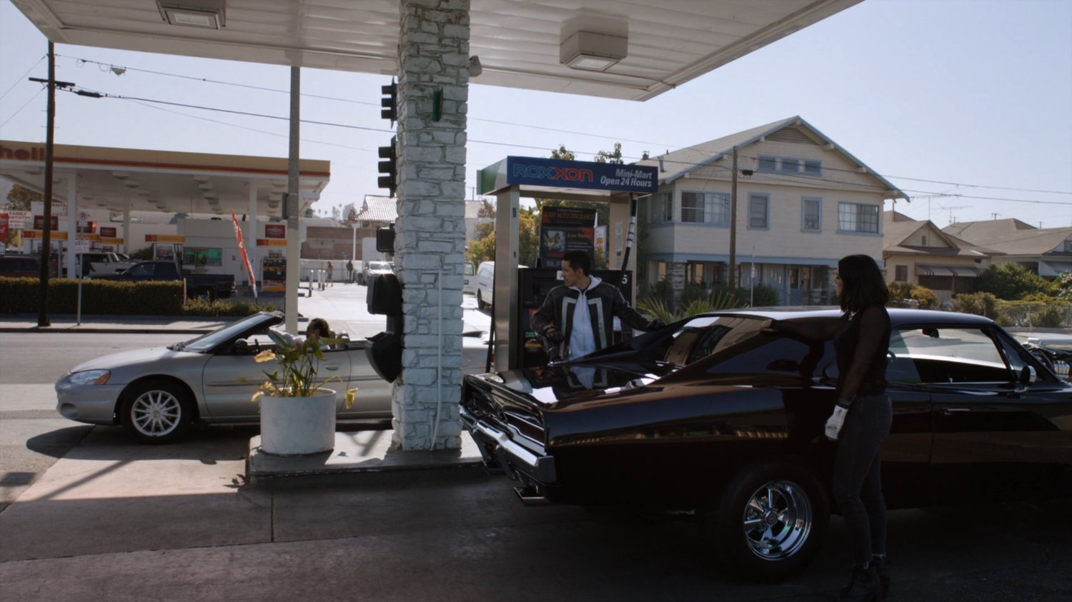 Daisy and Robbie outside black Charger at Roxxon gas station.