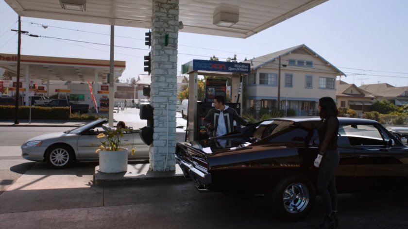Daisy and Robbie outside black charger at Roxxon gas station.