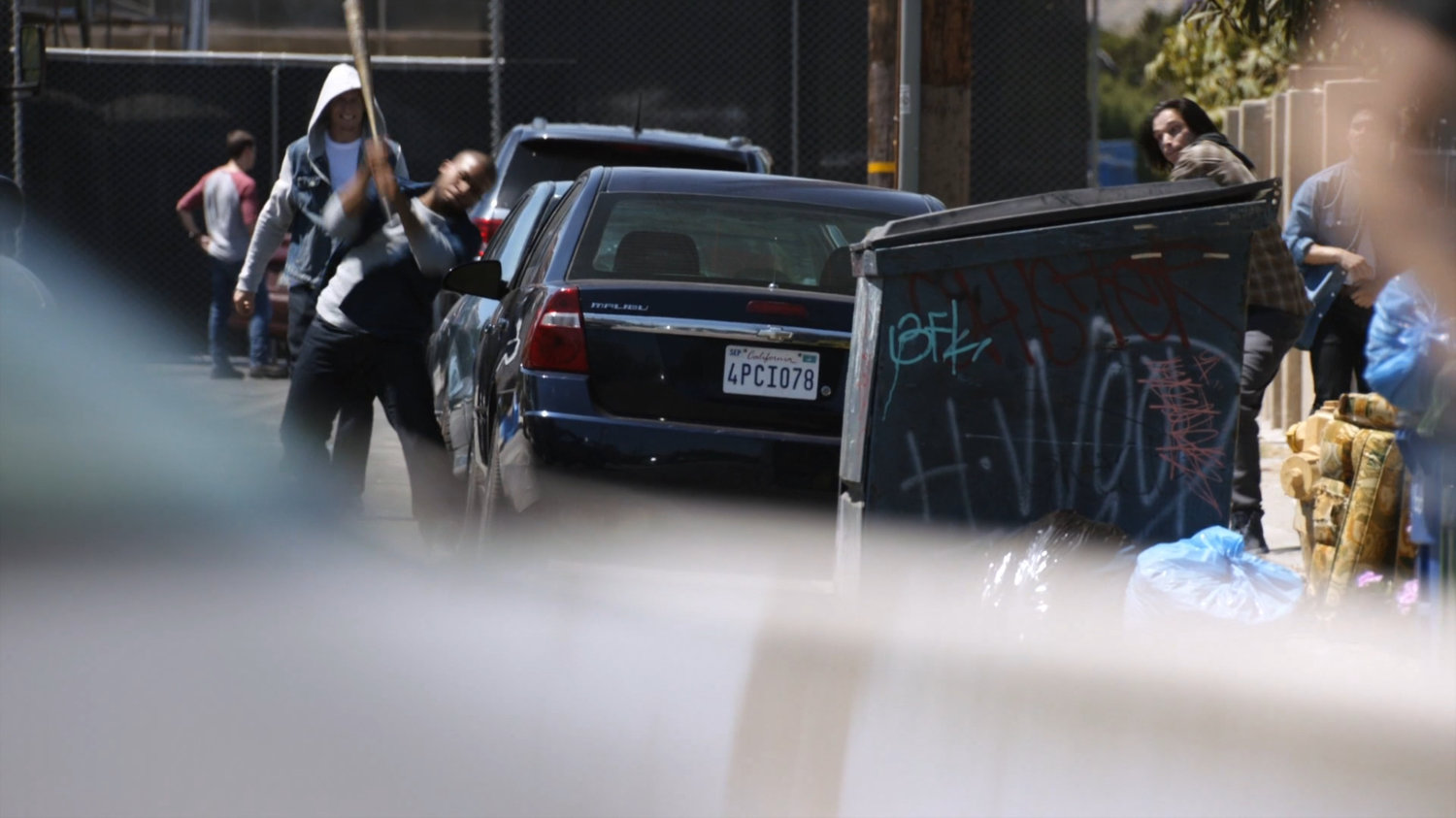 Rioters walking along street smashing cars with baseball bat.