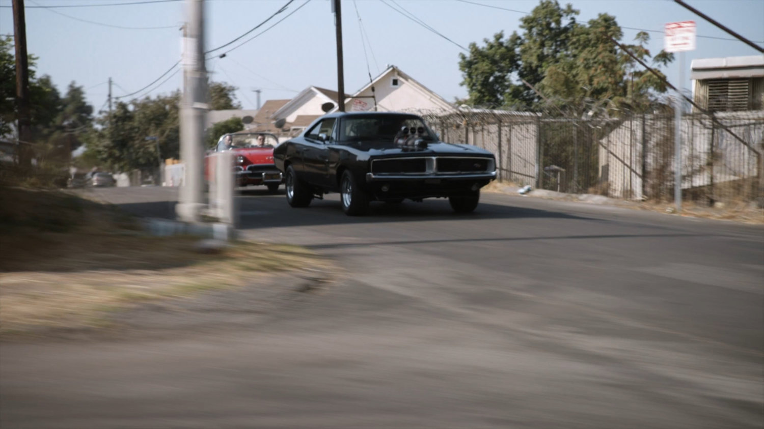Lola chasing black Charger along street.