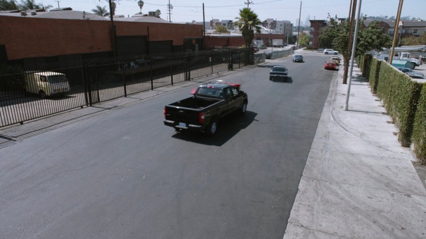 High angle view of Lola chasing black Charger along street.