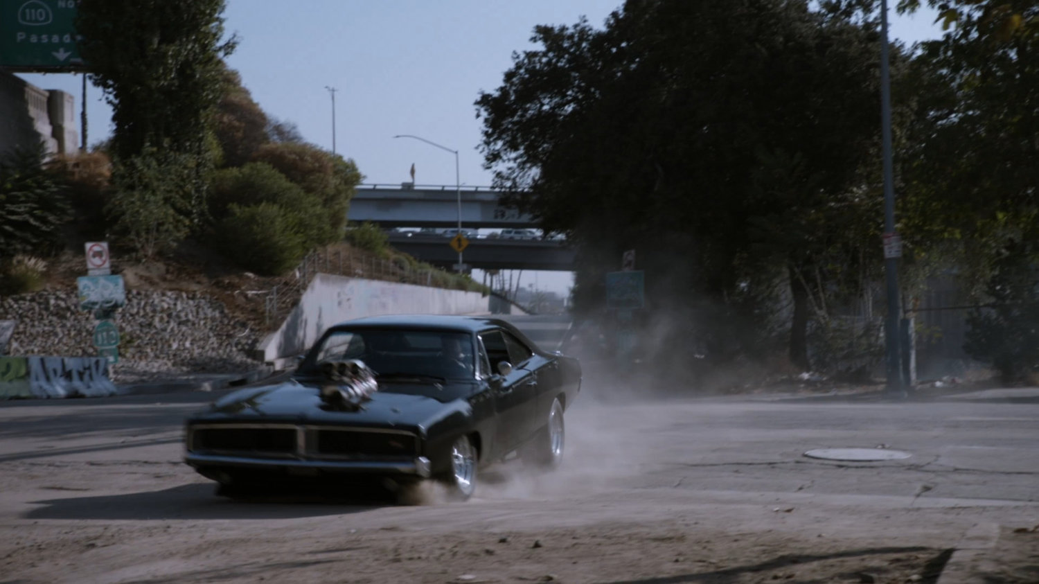 Black Charger skidding past freeway entrance.