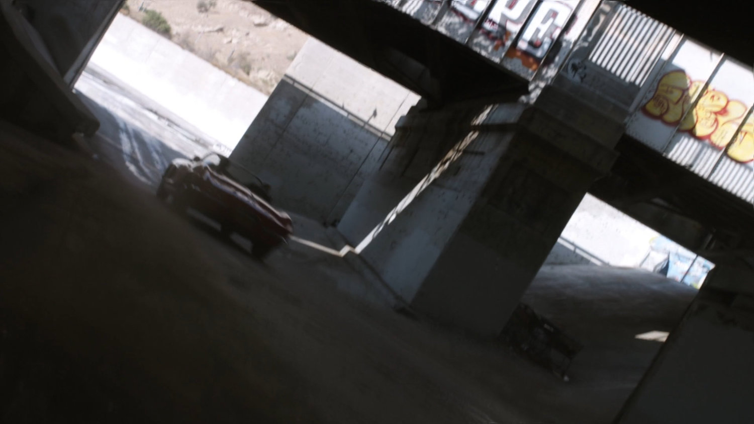 Lola chasing black Charger along river culvert.