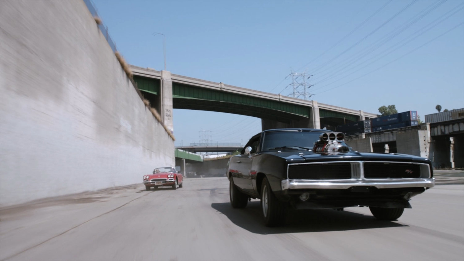 Lola chasing black Charger along river culvert.