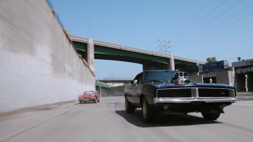 Lola chasing black Charger along river culvert.