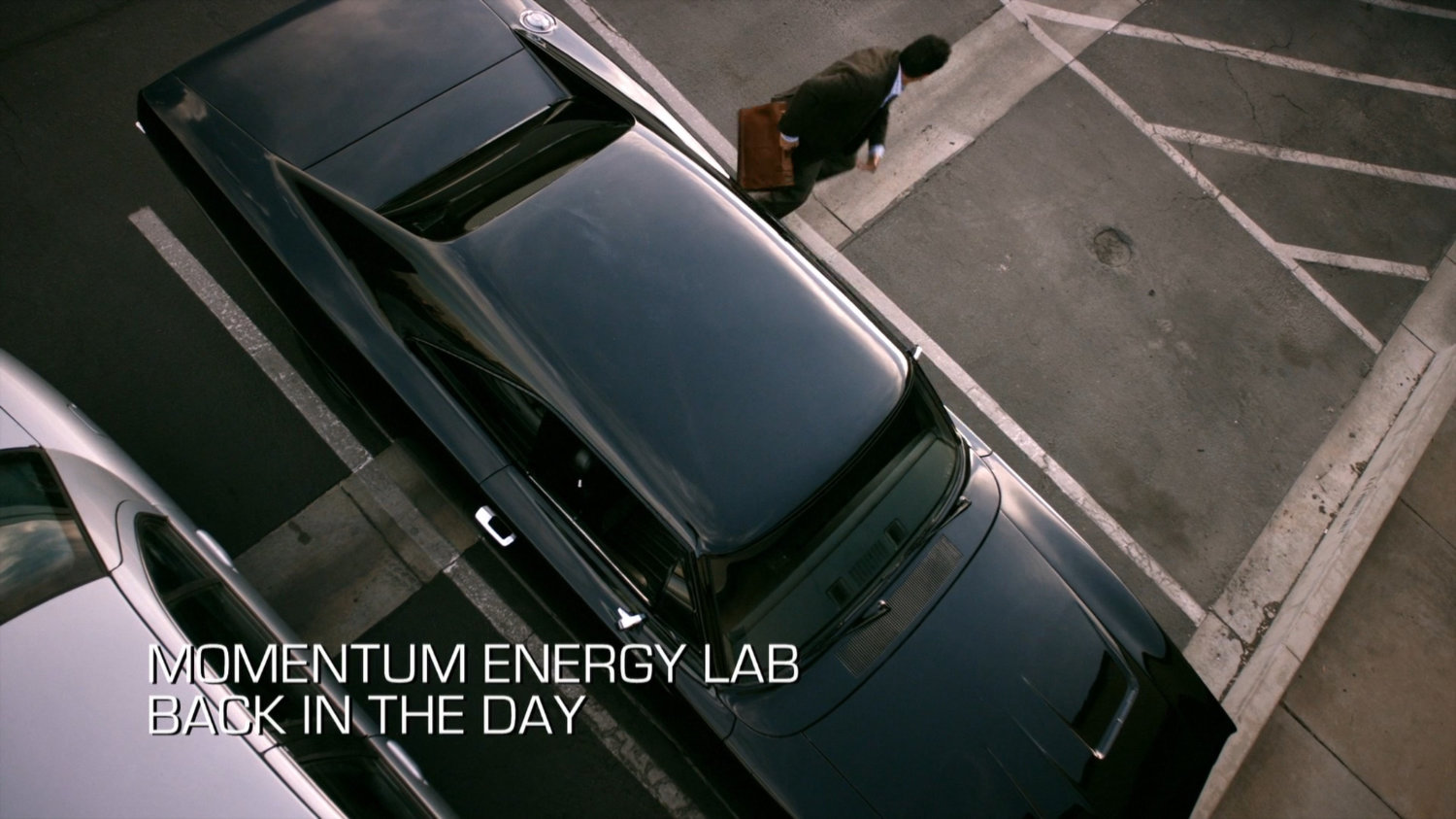 Eli exiting black Charger in parking lot of Momentum Labs. Text: Momentum Energy Lab, Back in the Day.