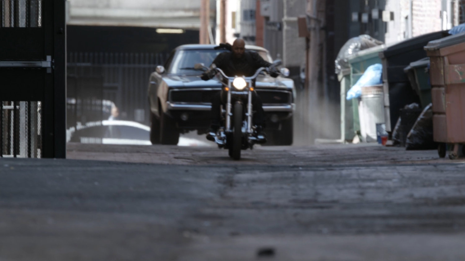 Mack on his motorcycle and black Charger in an alley in Los Angeles.