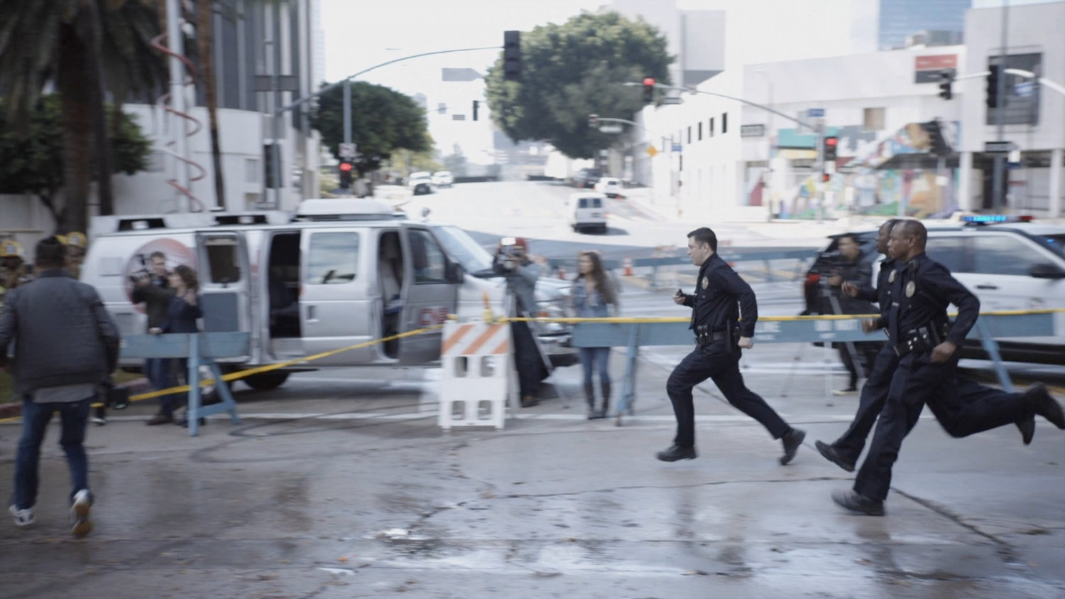 Officers run past a police barricade with onlookers and reporters gathered around.