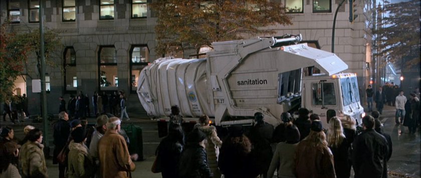 A crowd looks at a garbage truck at a New York intersection.