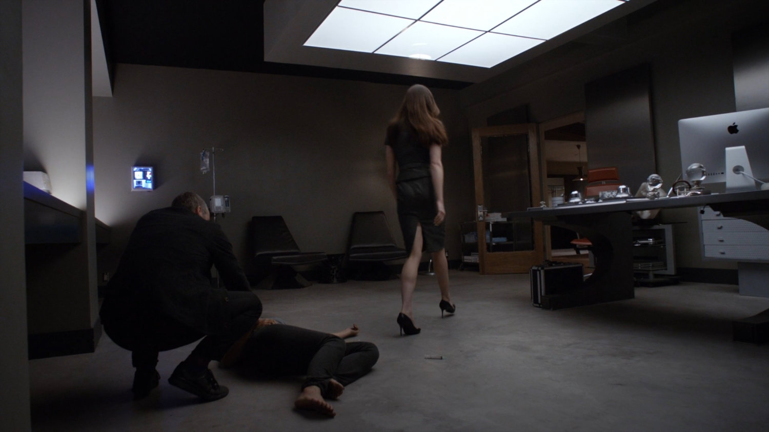 Radcliffe crouching over an unconscious May as Aida walks away.