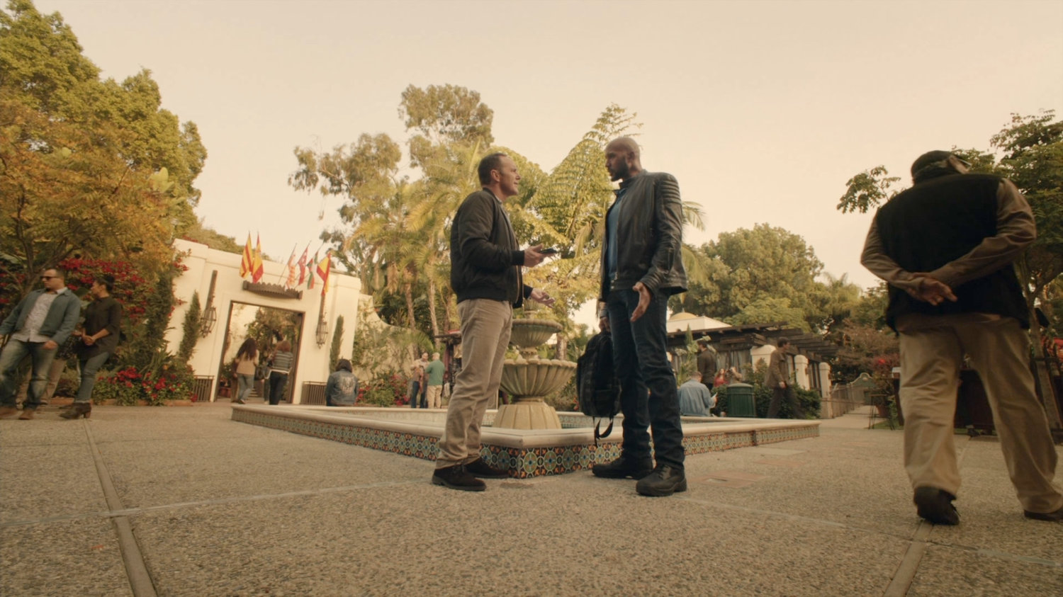 Coulson talks with Mack by fountain in Spanish plaza.