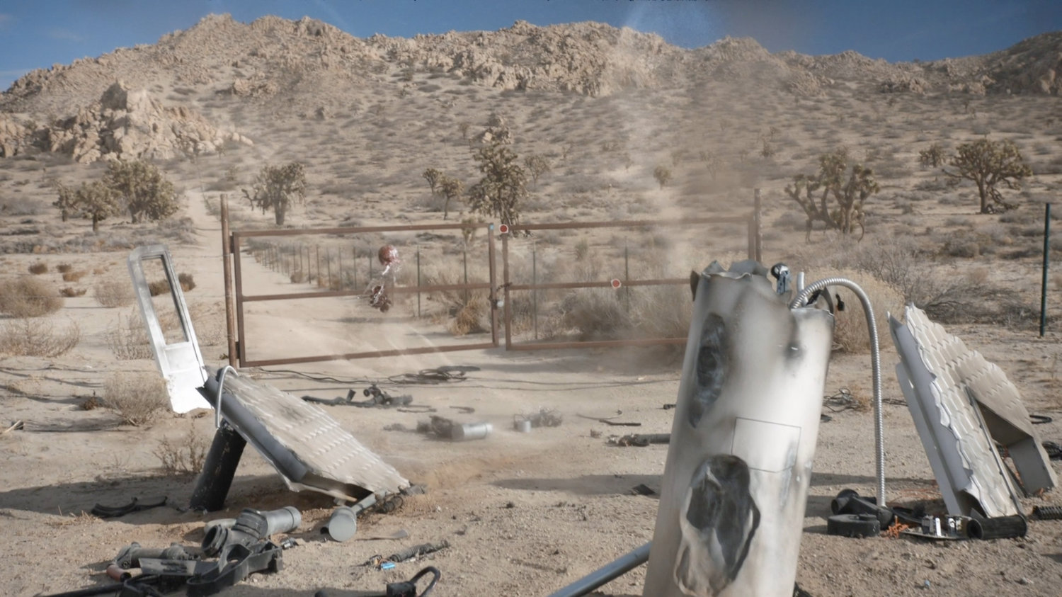 Shockley's body reforms outside rusted gates in the desert.