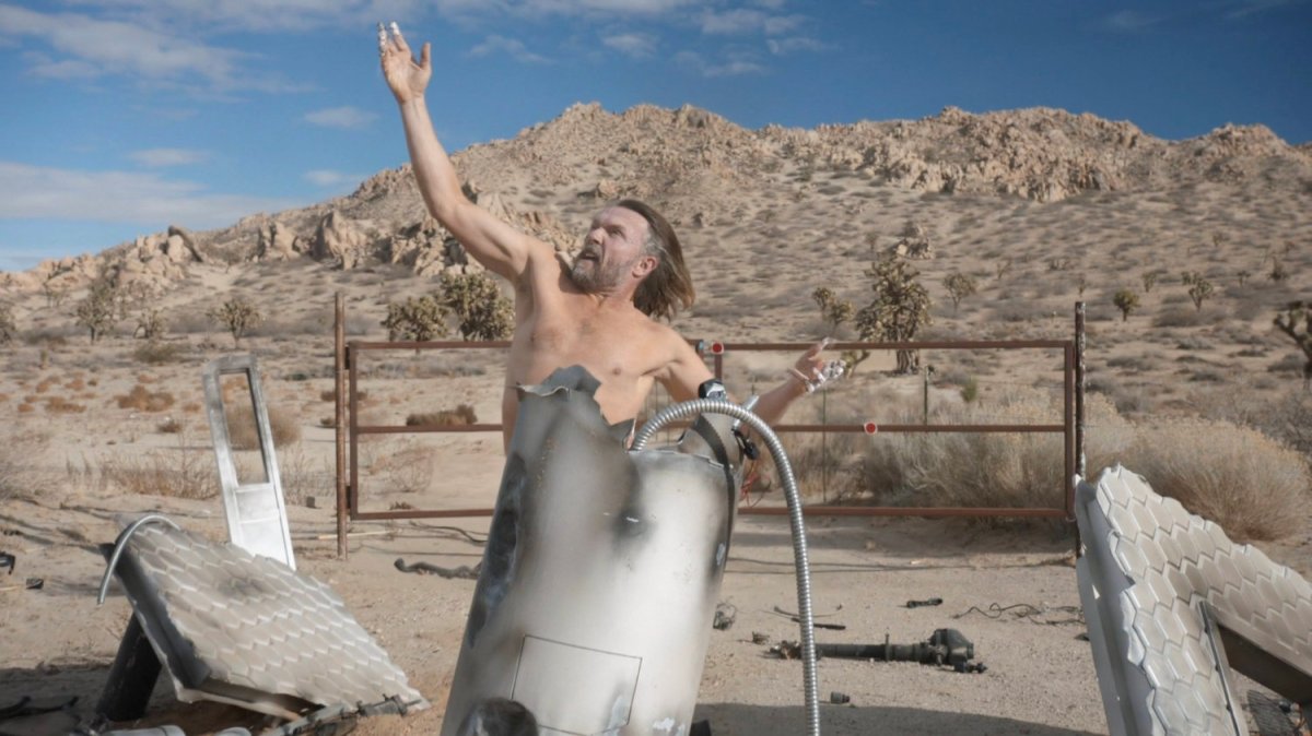 Shockley's body reforms outside rusted gates in the desert.