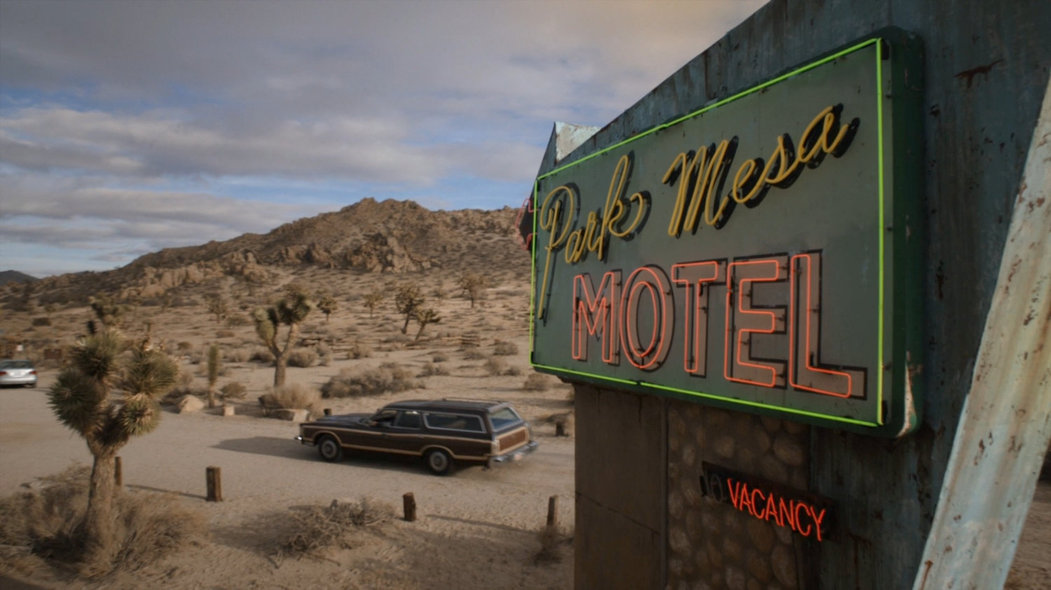 Station wagon driving past Park Mesa Motel sign.