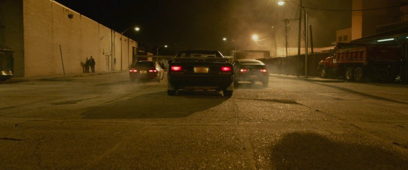 Three cars driving out of a parking lot for a street race.