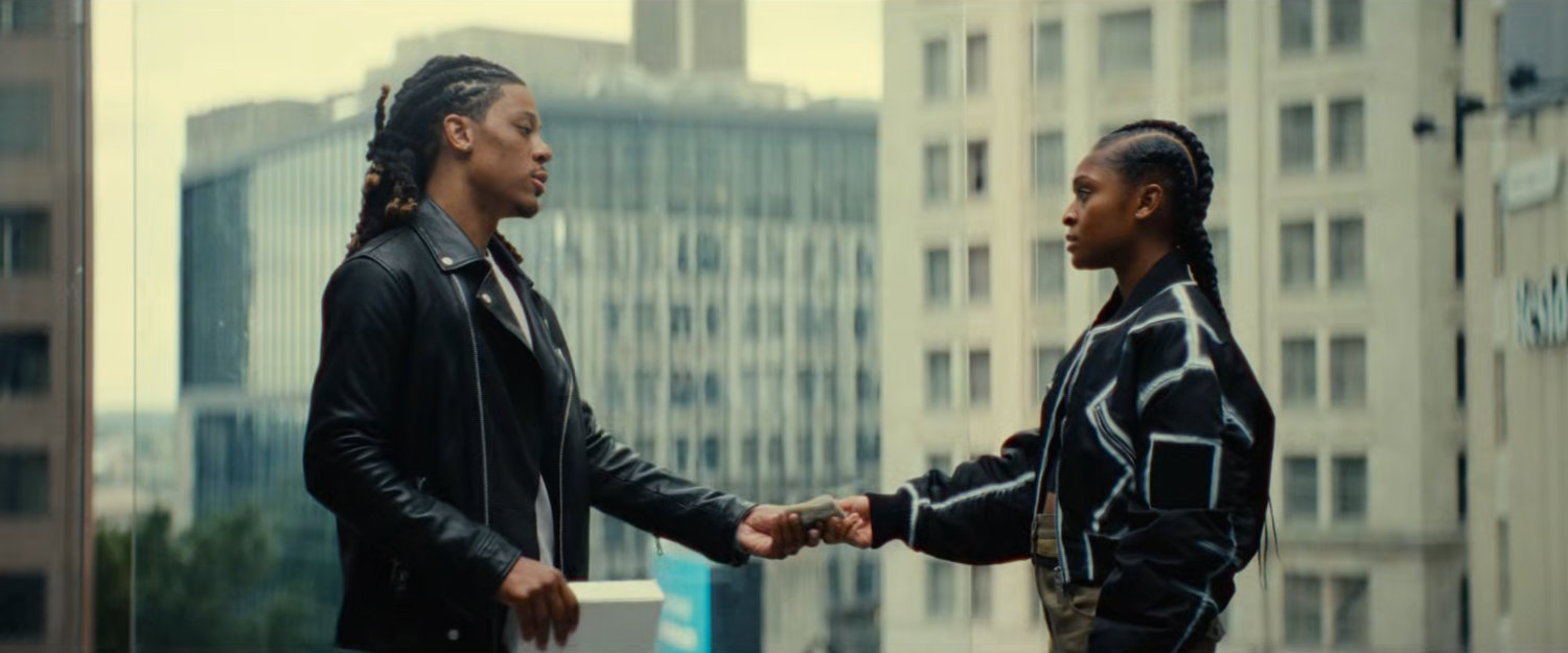Riri taking money from a man by a large window with downtown outside.