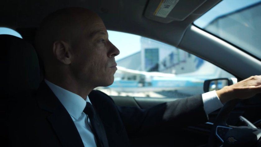 Enoch driving past an airport hangar.