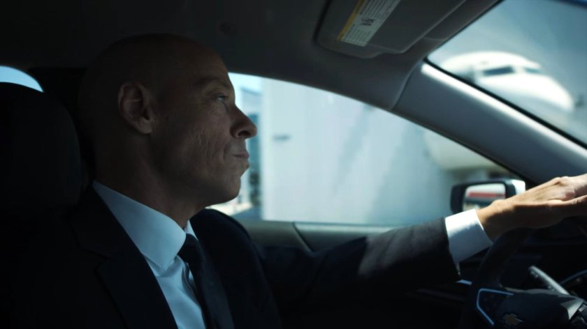 Enoch driving past an airport hangar.